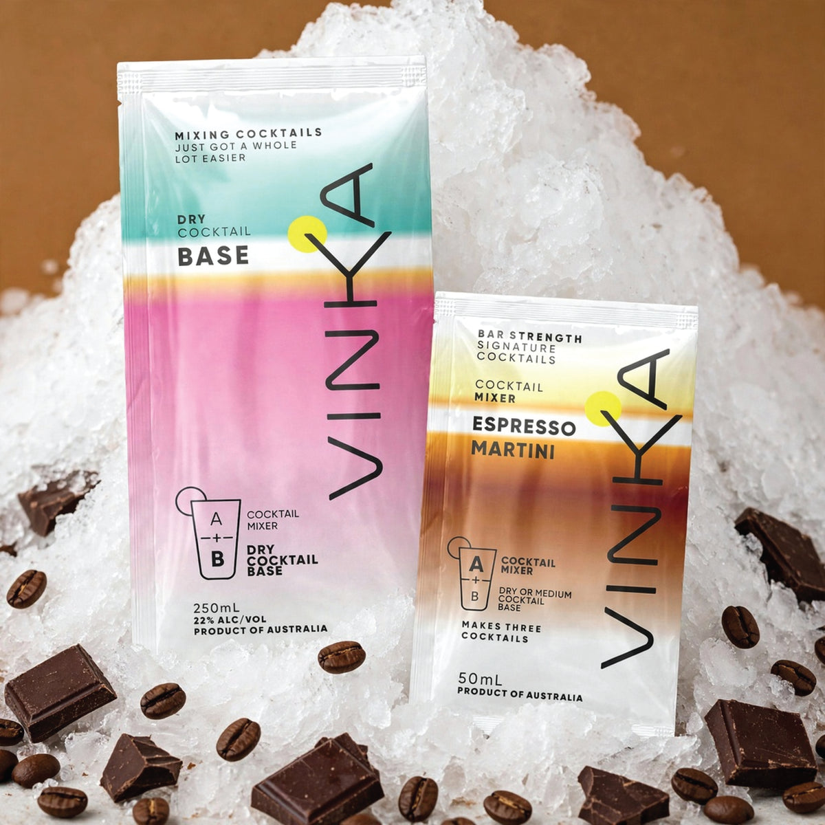 Two VINKA dry cocktail base mix packets, one labeled 'Dry Cocktail Base' and the other 'Espresso Martini', displayed on a bed of crushed ice with chocolate pieces scattered around on a warm brown background.