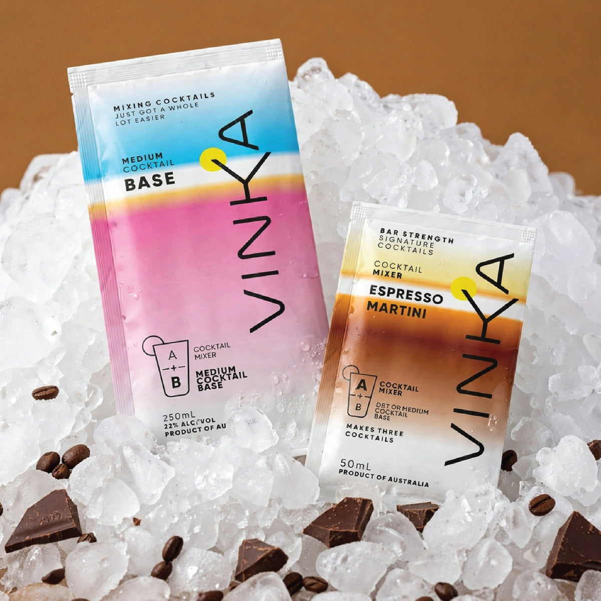 Two VINKA cocktail mix sachets, one labeled 'Medium Cocktail Base' and the other 'Bar Strength Cocktail Mixer Espresso Martini', displayed on crushed ice with chocolate chunks against a warm brown background.
