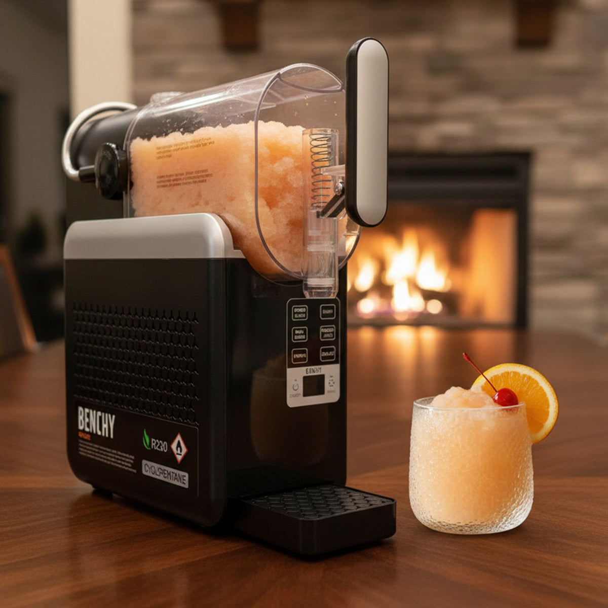 A Benchy Slushy Machine filled with Frozen Skinny Amaretto Sour VINKA Slushy Cocktail Kit (2L), shown on a wooden table in front of a lit fireplace, with a matching drink in a glass and orange slice garnish on the right.