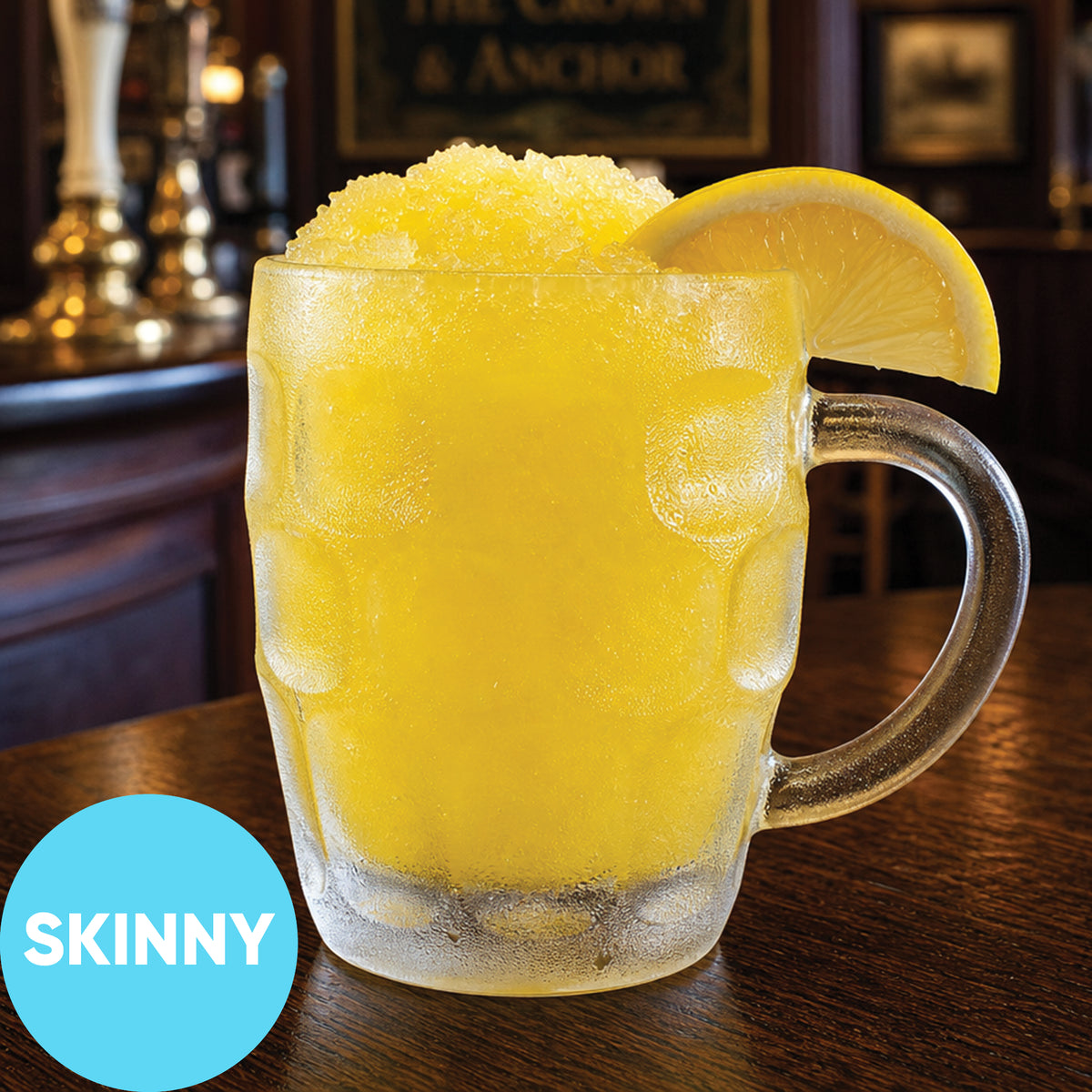 A frosted glass mug filled with a bright yellow slushy drink, garnished with a lemon slice, sitting on a wooden bar counter in a pub setting. A blue circular badge in the lower-left corner reads 'SKINNY'.